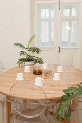 Cozy dining setting featuring a round wooden table surrounded by transparent chairs, complemented by lush green potted plants, creating a warm and inviting interior atmosphere.