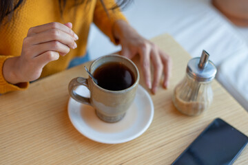 Latin woman adding sugar to her coffee at cafe table
