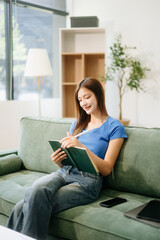 Obraz premium Young asian woman relax on comfortable couch at home texting messaging on smartphone and tablet smiling girl