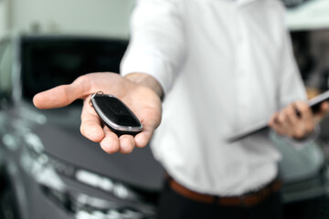 The car dealer hands the car keys to the camera in a modern car dealership. Concept a moment of trust and significance, emphasizing the importance of choosing the right vehicle.