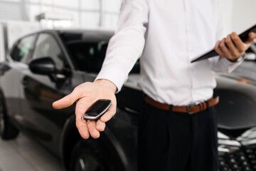 The car dealer hands the car keys to the camera in a modern car dealership. Concept a moment of trust and significance, emphasizing the importance of choosing the right vehicle.