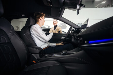 A car sales manager shows a vehicle to a customer in a luxurious dealership. Concept a premium...