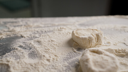 Professional baker kneading and flattening cookie dough on floured surface, showcasing culinary expertise in kitchen workspace
