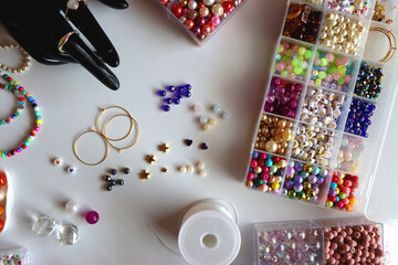 Hand figurine, colorful friendship bracelets, necklaces, various beads and DIY supplies on the table. Making jewelry at home. Flat lay.