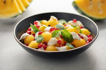 Summer fresh salad with yellow watermelon, pomegranate grains,, ricotta, and mint leaves in  bowl on the table.