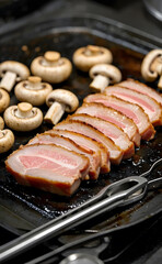 Slices of pork belly and mushrooms are grill on a metal griddle.