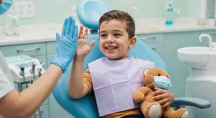 A cheerful boy with a teddy bear celebrates with a high five at the dentist