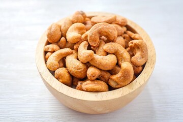 Salted cashew nuts in wooden bowl on white background	