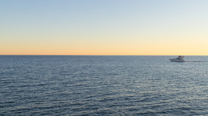 A peaceful scene of a small boat on a calm ocean at sunset, evoking serenity and solitude.