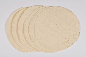 Round, flat tortillas are neatly stacked on a light background, showcasing their uniform shape and texture