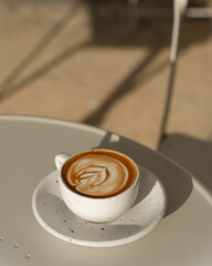 A latte with foam art in a textured ceramic cup, set against a neutral backdrop.