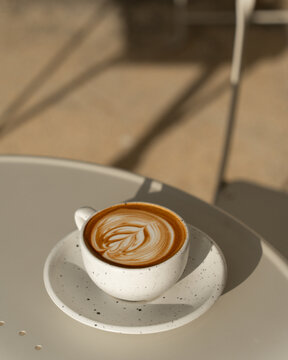 A latte with foam art in a textured ceramic cup, set against a neutral backdrop.