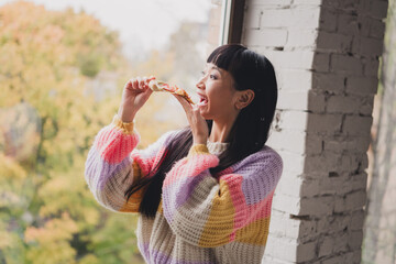 Obraz premium Young Woman Enjoying a Slice of Pizza by a Window Overlooking an Autumnal Scene