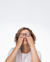 An exhausted woman with glasses rubs her eyes while wearing a white t-shirt against a plain background. Perfect for eye care, fatigue relief, and healthcare product promotions, highlighting the