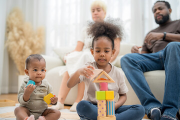 Siblings and family engage in playful building activity with colorful blocks in a cozy living room...