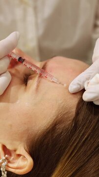 A close-up view of a doctor's gloved hands carefully administering a Botox injection into a young woman&rsquo;s forehead using a syringe. 
