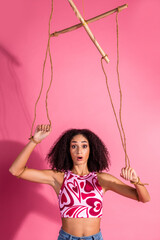 Young stylish woman with curly hair in a vibrant print top posing against a pink vertical background
