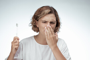 A woman in a white t-shirt covers her mouth and holds a toothbrush, showing signs of discomfort....