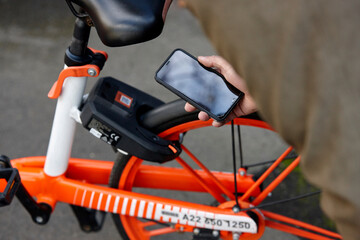 Man using mobile phone to unlock two-wheeled bike-sharing vehicle in city