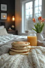 Breakfast in bed stack of pancakes, orange juice, tulips on cozy blanket