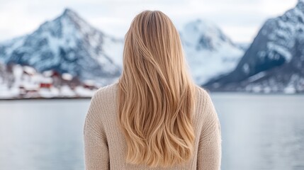 Fototapeta premium A woman with long hair gazes out over a serene lake, surrounded by majestic snow-capped mountains and a clear sky.