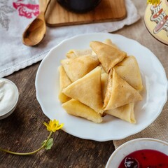 Pancakes with cottage cheese and sour cream in a plate on a wooden background. Sweet pancakes with filling. Ukrainian national cuisine. Sweet rolls with cottage cheese 