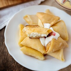 Pancakes with cottage cheese and sour cream in a plate on a wooden background. Sweet pancakes with filling. Ukrainian national cuisine. Sweet rolls with cottage cheese 