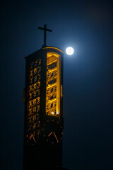 Nighttime view of a church tower illuminated under a full moon with a serene sky backdrop