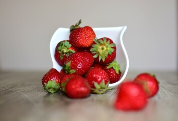 Fresh strawberries spilled out from the bowl on a wooden table. Strawberries close up macro.
