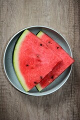 Fresh watermelon two slices in the plate on the wooden table top view. Red juicy fruit in plate plain shot.