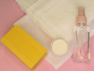 Laundry accessories on pink background. A white laundry bag and towel, a spray bottle, a container with baking powder and a soap bar on pink background.