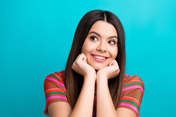 Smiling young woman in a striped colorful outfit posing against a teal background, looking cheerful...