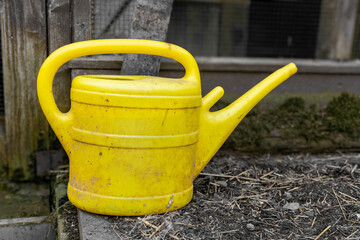 Fototapeta premium Bright yellow watering can resting on a garden edge during a cloudy day in early spring
