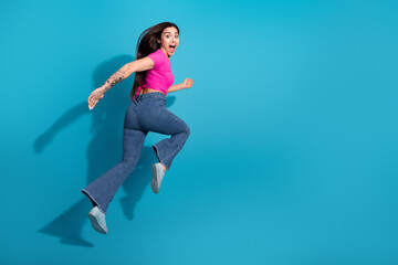 Energetic young woman in vibrant outfit jumping joyfully against a bold blue background