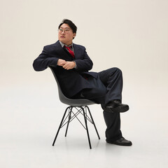 Businessman, Asian guy, dressed formal attire looking away, sitting on chair and exuding confidence...