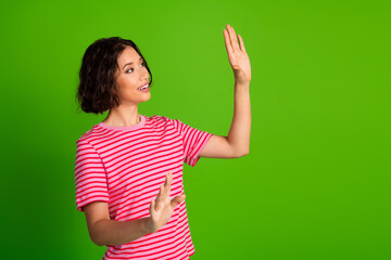 Happy young woman wearing a striped pink t-shirt making expressive hand gestures against a vibrant green studio background