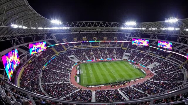 Wide-angle shot of a vibrant, packed stadium at night, capturing the excitement of a live sports event, perfect for a dynamic video backdrop.
