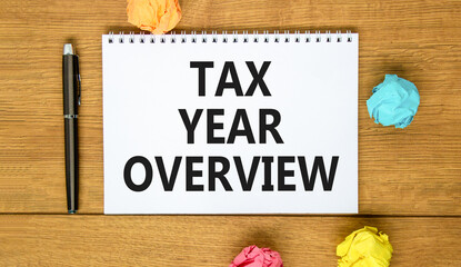 Tax year overview symbol. Concept words Tax year overview on beautiful white note. Beautiful wooden background. Black pen. Colored paper. Business tax year overview concept. Copy space.