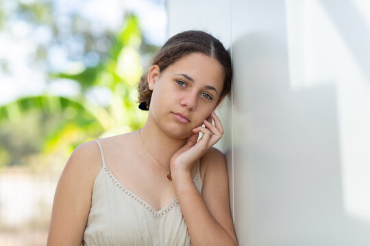 Teenage girl with hand to face leaning against white wall