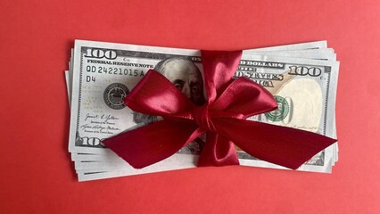Stack of 100-dollar bills tied with a red ribbon, cash gift concept on red background