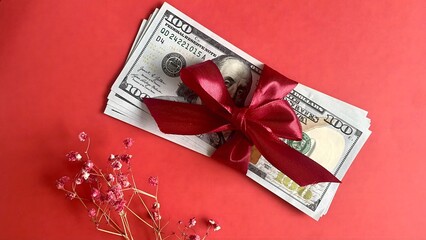 Cash gift of 100-dollar bills with red ribbon and pink gypsophila on red background