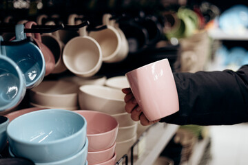 Man holding pink ceramic cup from a shelf in homeware store.