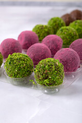 Two types of chocolate candies with sprinkles of ground pistachios and pitahaya powder on a light background. Dessert for a holiday. Handmade. Close-up