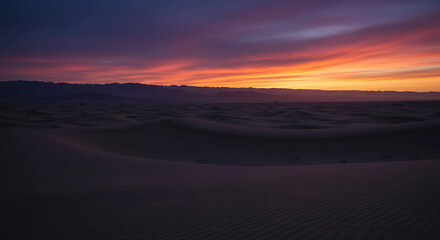 Desert landscape with a vibrant sunset sky above dunes