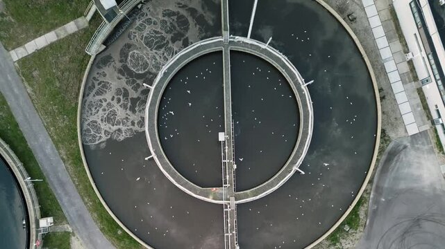 Top-down aerial shot of a large circular water treatment plant. Focus on industrial infrastructure, wastewater management, and sustainable utilities.