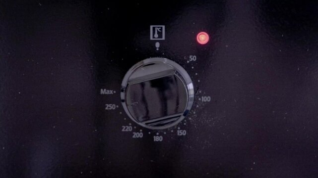 Close-up of hand turning control knob on oven panel. Fingers grasp and adjust silver dial with temperature markings visible. Everyday cooking, home appliance usage, culinary preparation.