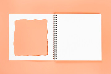 White notebook with cut-out frame on the page. Blank layout template of spiral notebook on pink background.