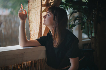 A woman sits introspectively by a sunlit window, surrounded by lush greenery, conveying a sense of...