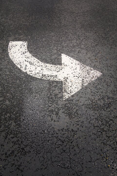 A white painted curving arrow symbol, a road marking on a road surface.