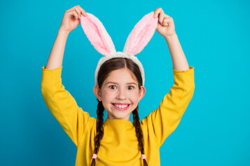 Cheerful young girl in yellow sweater with bunny ears posing against blue background, symbolizing playfulness, joy